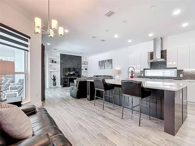 kitchen with wall chimney exhaust hood, modern cabinets, light wood-type flooring, white cabinetry, and a kitchen bar