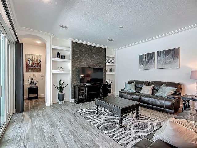living area with a textured ceiling, light wood-style flooring, crown molding, built in shelves, and baseboards
