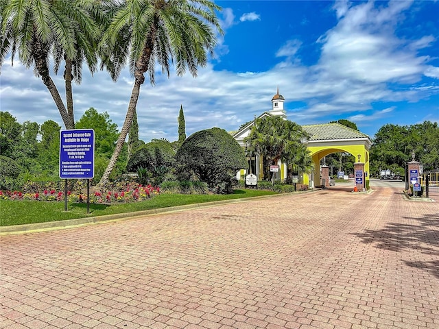 view of decorative road featuring curbs, street lights, and a gated entry