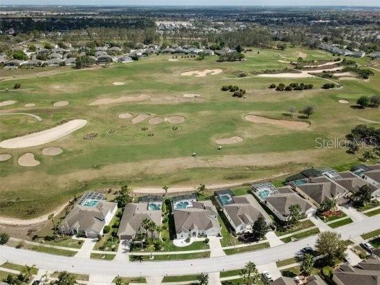 aerial view of property and surrounding area featuring a golf course and nearby suburban area