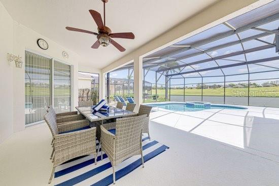 view of pool featuring a patio area, ceiling fan, a pool with connected hot tub, glass enclosure, and outdoor dining space
