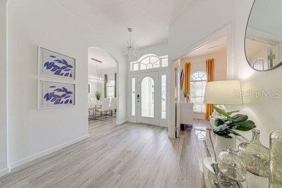 entrance foyer with wood finished floors, arched walkways, a chandelier, and baseboards