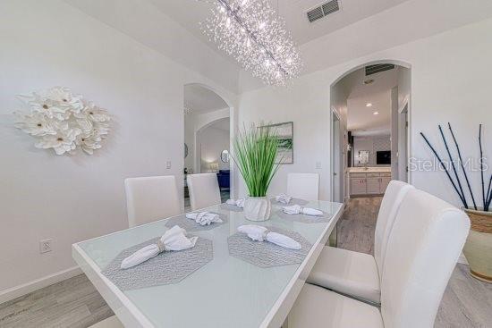 dining area with arched walkways, light wood-style floors, baseboards, and a chandelier