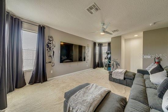 living room featuring carpet floors, ceiling fan, a textured ceiling, and baseboards