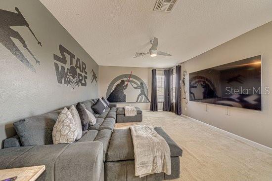 carpeted living room with a textured ceiling, ceiling fan, and baseboards