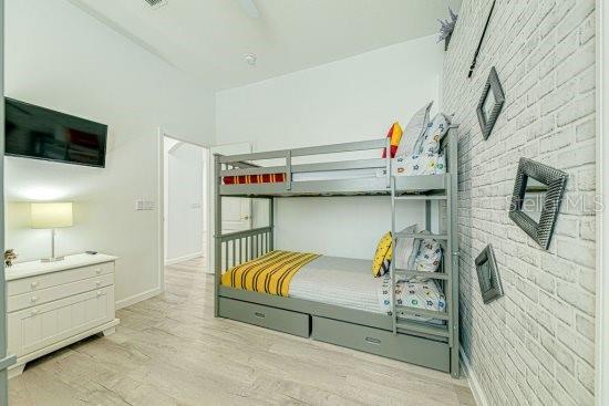 bedroom featuring light wood-style flooring, brick wall, and baseboards
