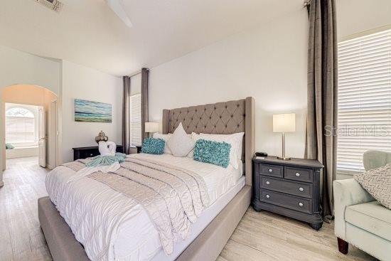 bedroom with light wood finished floors, arched walkways, and ensuite bath