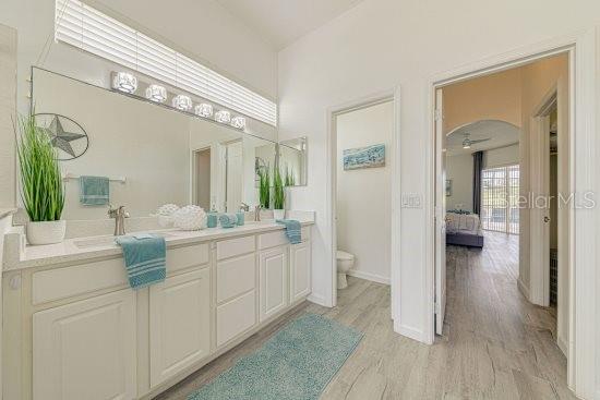 ensuite bathroom featuring toilet, wood finished floors, double vanity, and baseboards