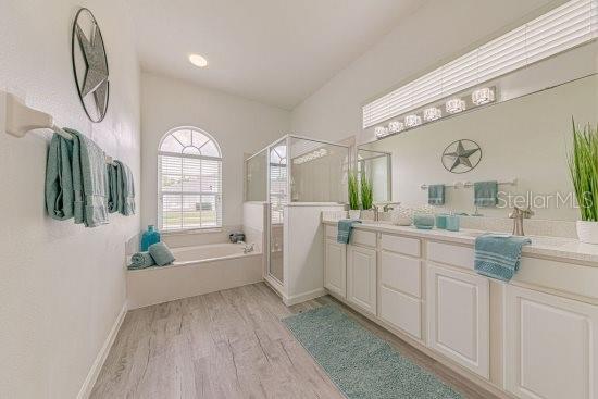 full bathroom with wood finished floors, a shower stall, a garden tub, vanity, and baseboards