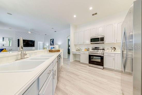 kitchen with appliances with stainless steel finishes, a sink, white cabinets, light wood-style floors, and recessed lighting