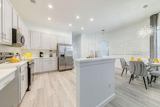 kitchen featuring appliances with stainless steel finishes, light wood-style floors, light countertops, recessed lighting, and an island with sink
