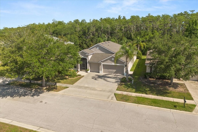 view of front of home with concrete driveway, stucco siding, a front lawn, an attached garage, and a wooded view