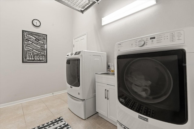 clothes washing area featuring washer and clothes dryer, light tile patterned floors, cabinet space, and baseboards