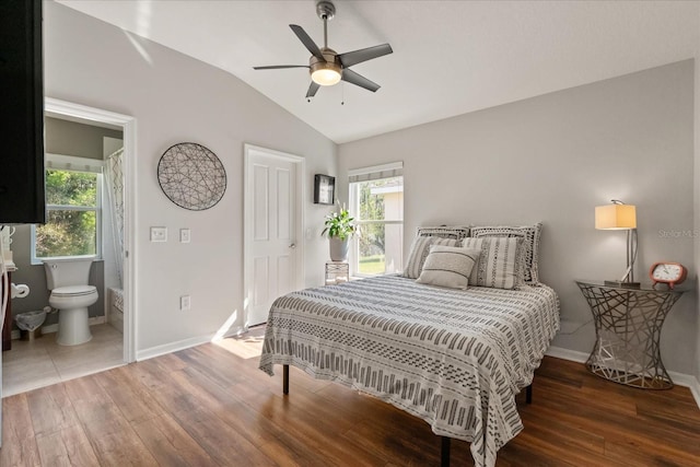 bedroom featuring lofted ceiling, wood finished floors, baseboards, and ensuite bath