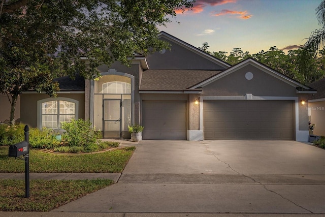 view of front facade with stucco siding, an attached garage, concrete driveway, and a shingled roof
