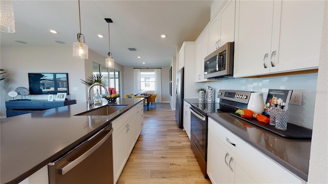 kitchen featuring stainless steel appliances, a sink, dark countertops, light wood-style floors, and white cabinetry