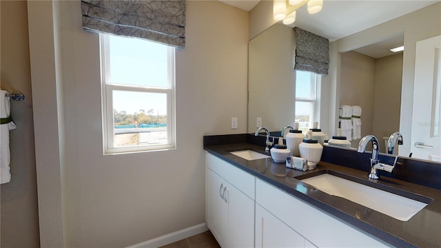bathroom featuring healthy amount of natural light, double vanity, and baseboards