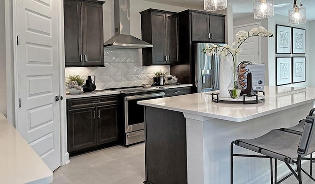 kitchen featuring wall chimney exhaust hood, appliances with stainless steel finishes, a kitchen breakfast bar, light countertops, and decorative backsplash