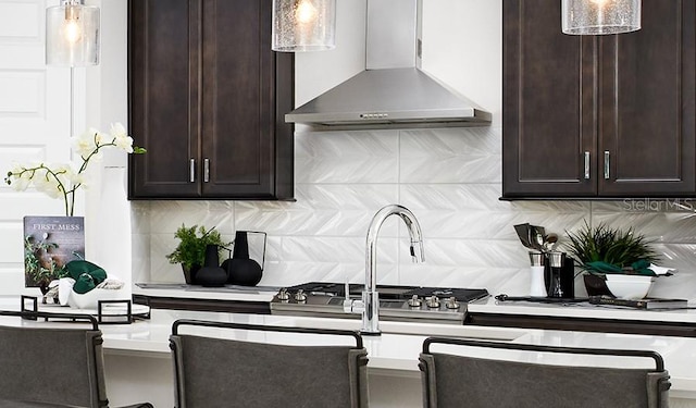 kitchen with wall chimney range hood, dark brown cabinetry, pendant lighting, light countertops, and backsplash