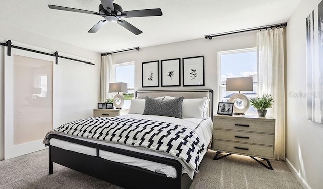carpeted bedroom featuring a barn door, a ceiling fan, and baseboards