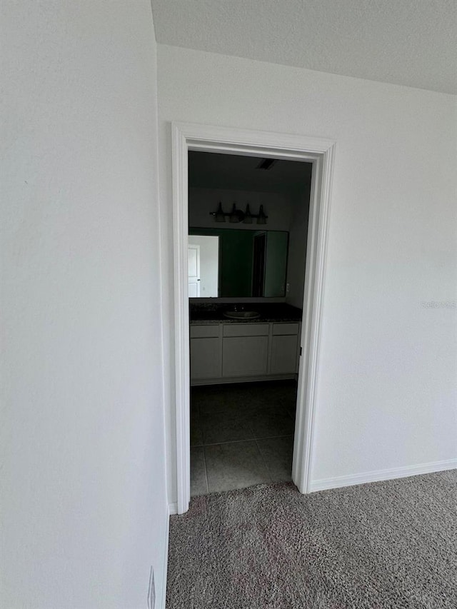 hallway with dark carpet, a sink, baseboards, and dark tile patterned flooring