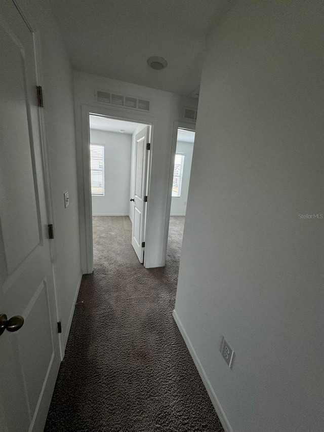 corridor featuring dark carpet and baseboards