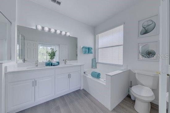 2908 Sunset Lakes Blvd, Kissimmee, FL 34747 - bathroom with wood finished floors, a garden tub, double vanity, and toilet