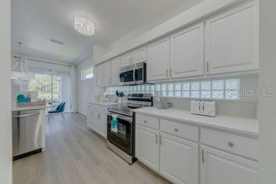 2908 Sunset Lakes Blvd, Kissimmee, FL 34747 - kitchen with stainless steel appliances, white cabinetry, light wood-style floors, and light countertops