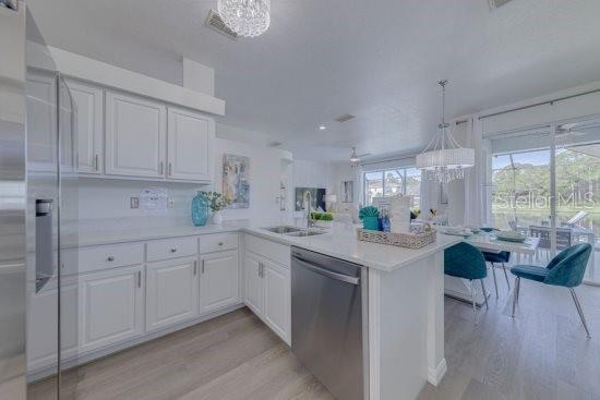 2908 Sunset Lakes Blvd, Kissimmee, FL 34747 - kitchen with stainless steel appliances, a sink, light wood-style floors, a peninsula, and white cabinetry