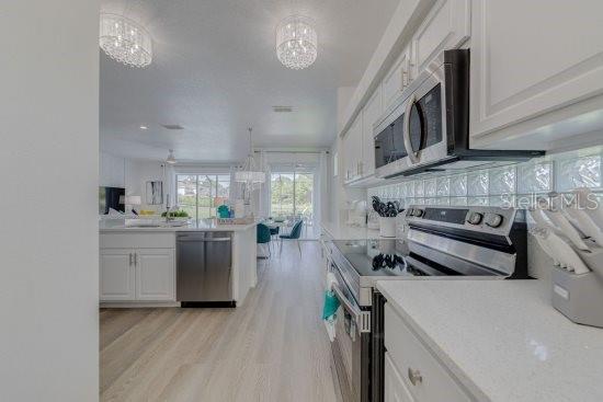 2908 Sunset Lakes Blvd, Kissimmee, FL 34747 - kitchen with appliances with stainless steel finishes, light wood-style flooring, white cabinets, a chandelier, and light countertops