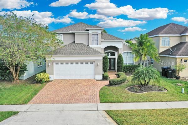 721 Hardwood Cir, Orlando, FL 32828 - view of front of house with decorative driveway, a garage, stucco siding, a front lawn, and a shingled roof