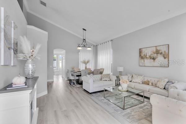 721 Hardwood Cir, Orlando, FL 32828 - living area featuring arched walkways, vaulted ceiling, light wood-style flooring, baseboards, and ornamental molding