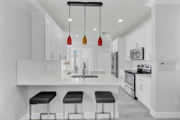 721 Hardwood Cir, Orlando, FL 32828 - kitchen with appliances with stainless steel finishes, a sink, white cabinetry, a peninsula, and a breakfast bar area