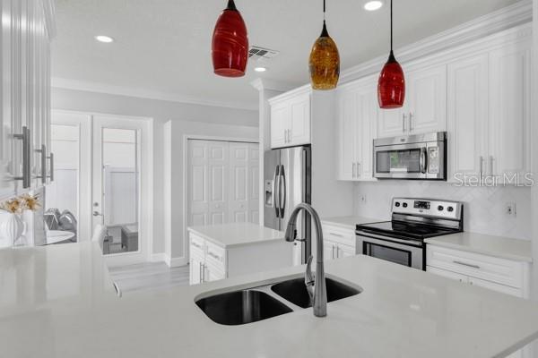 721 Hardwood Cir, Orlando, FL 32828 - kitchen featuring appliances with stainless steel finishes, a sink, white cabinets, light countertops, and hanging light fixtures