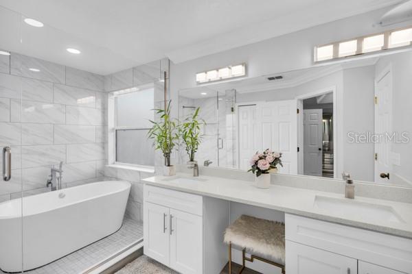 721 Hardwood Cir, Orlando, FL 32828 - bathroom with double vanity, a stall shower, a freestanding bath, recessed lighting, and plenty of natural light