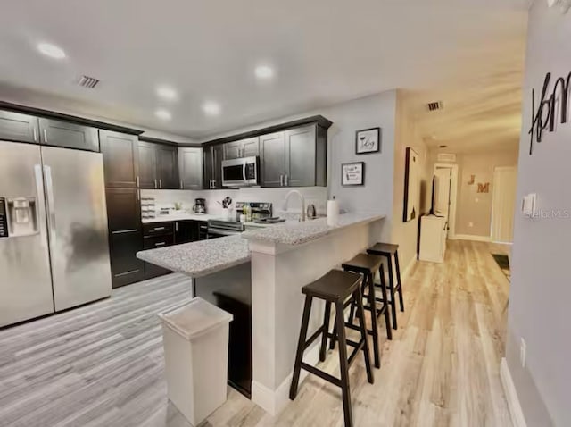 2798 Club Cortile Cir Unit A, Kissimmee, FL 34746 - kitchen with appliances with stainless steel finishes, a peninsula, a breakfast bar area, light wood finished floors, and light stone countertops
