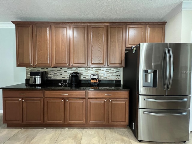 3003 Cobham Rd, Kissimmee, FL 34758 - kitchen with stainless steel refrigerator with ice dispenser, dark stone countertops, backsplash, brown cabinetry, and a textured ceiling