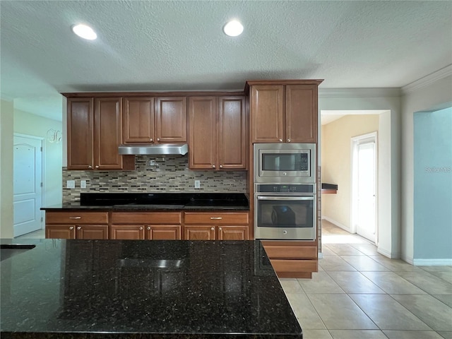 3003 Cobham Rd, Kissimmee, FL 34758 - kitchen featuring appliances with stainless steel finishes, under cabinet range hood, decorative backsplash, dark stone counters, and crown molding