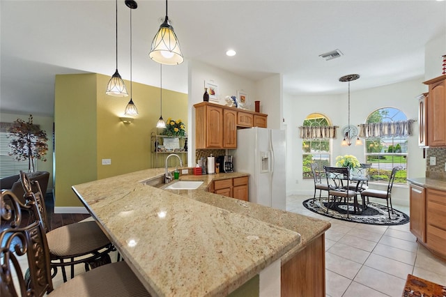 1258 Donalds Pl, The Villages, FL 32162 - kitchen with white fridge with ice dispenser, a sink, a peninsula, backsplash, and light stone countertops
