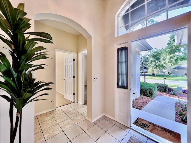 foyer entrance with arched walkways, light tile patterned floors, and baseboards