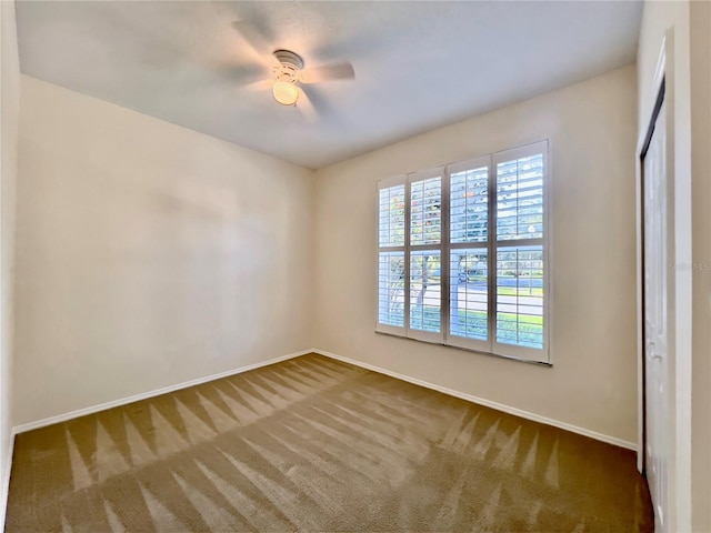 unfurnished room featuring baseboards, dark carpet, and ceiling fan