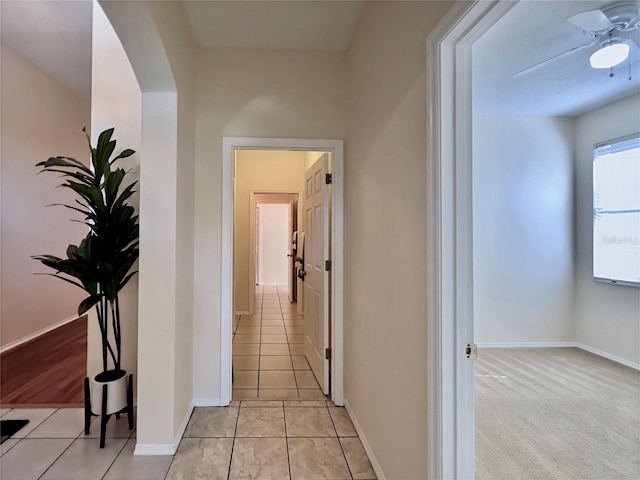 corridor featuring light tile patterned floors, baseboards, and arched walkways