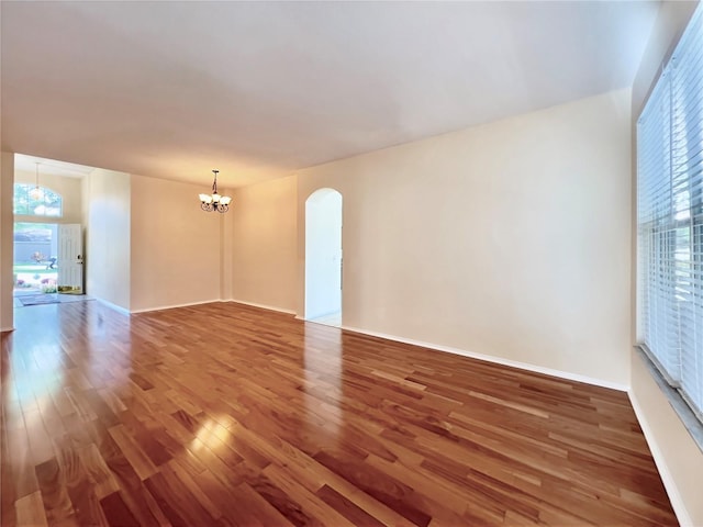 unfurnished room featuring a chandelier, wood finished floors, plenty of natural light, and arched walkways