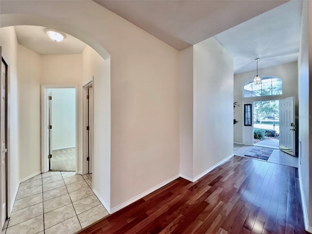 hall featuring arched walkways, baseboards, and light wood-style floors