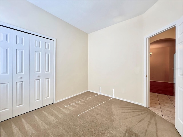 unfurnished bedroom with arched walkways, carpet, baseboards, and a closet