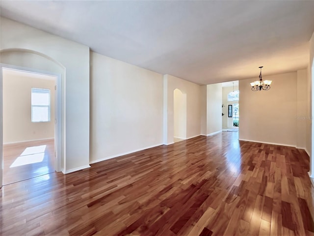 spare room featuring a chandelier, arched walkways, wood finished floors, and baseboards