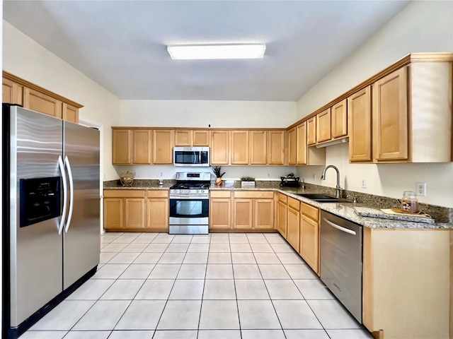 kitchen with appliances with stainless steel finishes, a sink, light tile patterned floors, light brown cabinets, and light stone countertops