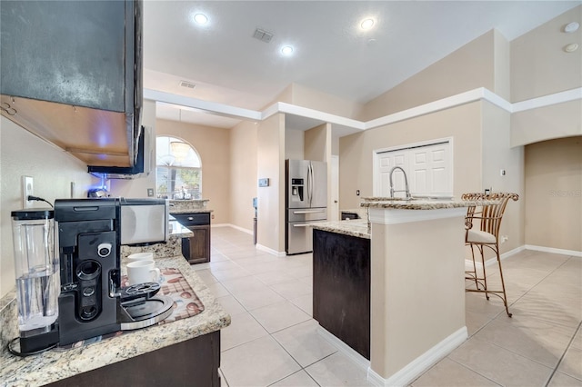 3211 Countryside View Dr, Saint Cloud, FL 34772 - kitchen featuring stainless steel fridge, light tile patterned floors, light stone countertops, a breakfast bar area, and a kitchen island with sink