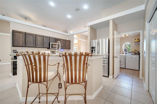 3211 Countryside View Dr, Saint Cloud, FL 34772 - kitchen featuring stainless steel appliances, independent washer and dryer, dark brown cabinets, a kitchen breakfast bar, and light tile patterned floors