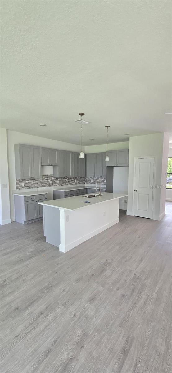 kitchen featuring gray cabinets, a sink, a kitchen island with sink, light wood-style floors, and a textured ceiling